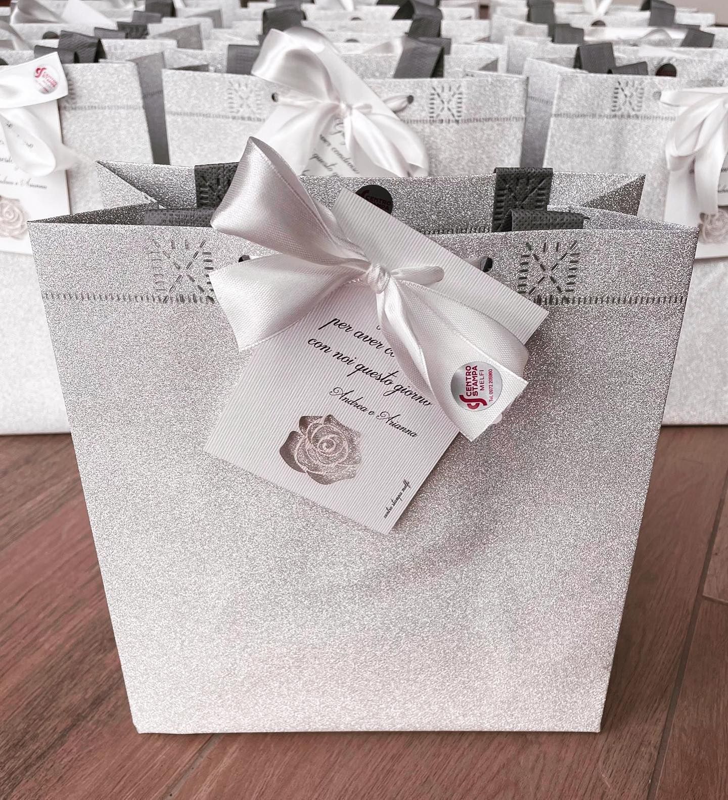 Sacchetto regalo argentato scintillante con nastro bianco ed etichetta. Altre borse sullo sfondo.