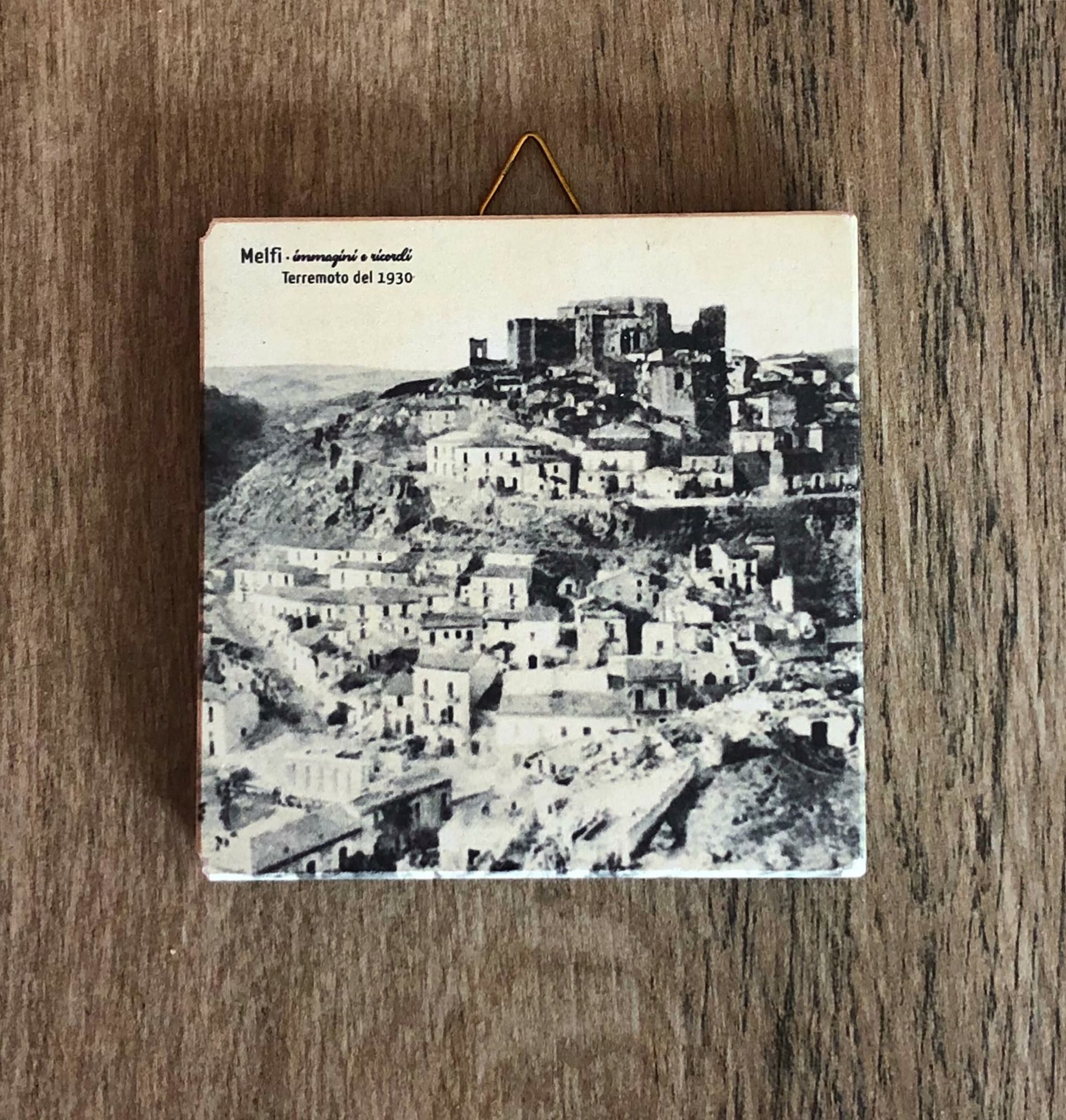 Piastrella in bianco e nero con la foto di una cittadina collinare. Sopra è scritto 