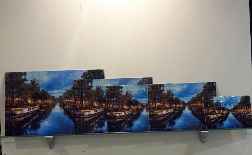 Una serie di opere d'arte incorniciate che raffigurano un corso d'acqua di notte, con luci che si riflettono sull'acqua, esposte su uno scaffale.