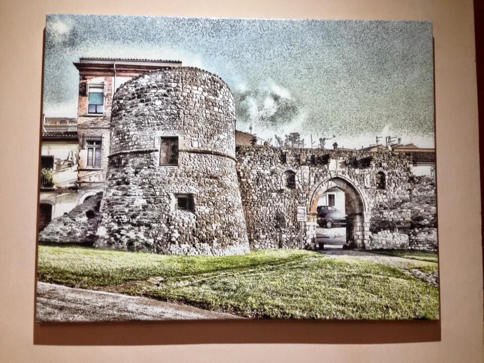 Torre in pietra e portale ad arco di un vecchio edificio, con erba verde di fronte e cielo nuvoloso.