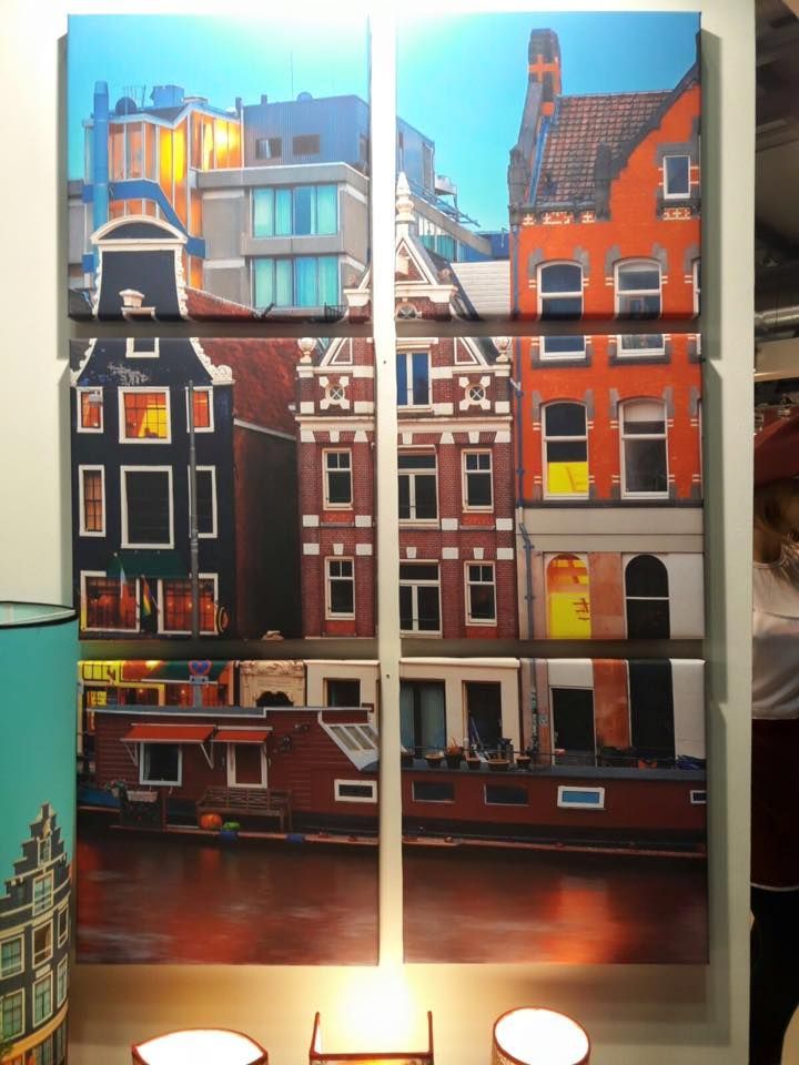 Quadro su tela multipannello raffigurante edifici di Amsterdam riflessi nell'acqua; cielo blu, tonalità arancioni e marroni.