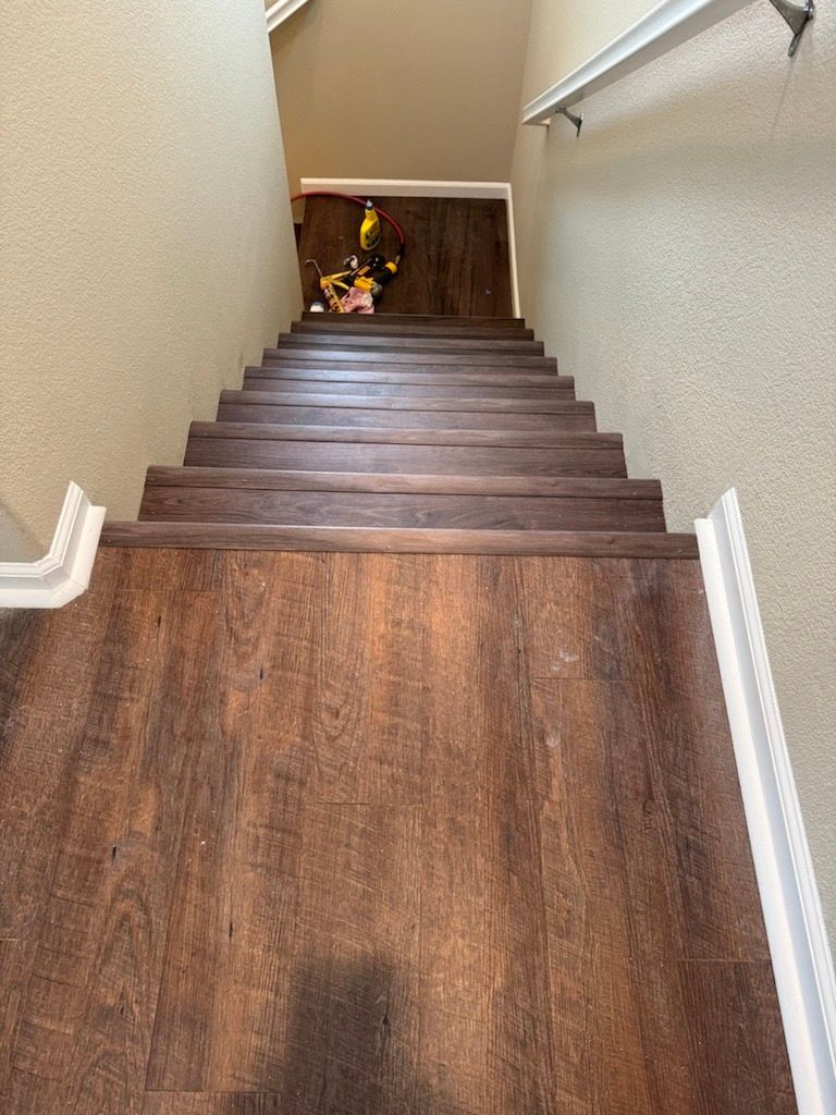 Staircase with wood-look flooring leading downwards. Tan walls with white trim and a handrail are visible.