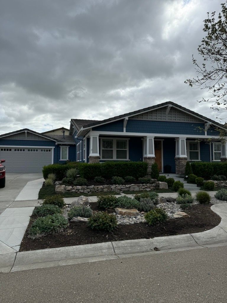 Blue house with gray trim and garage, front yard with landscaping under a cloudy sky. Blue house with gray trim and garage, front yard with landscaping under a cloudy sky.