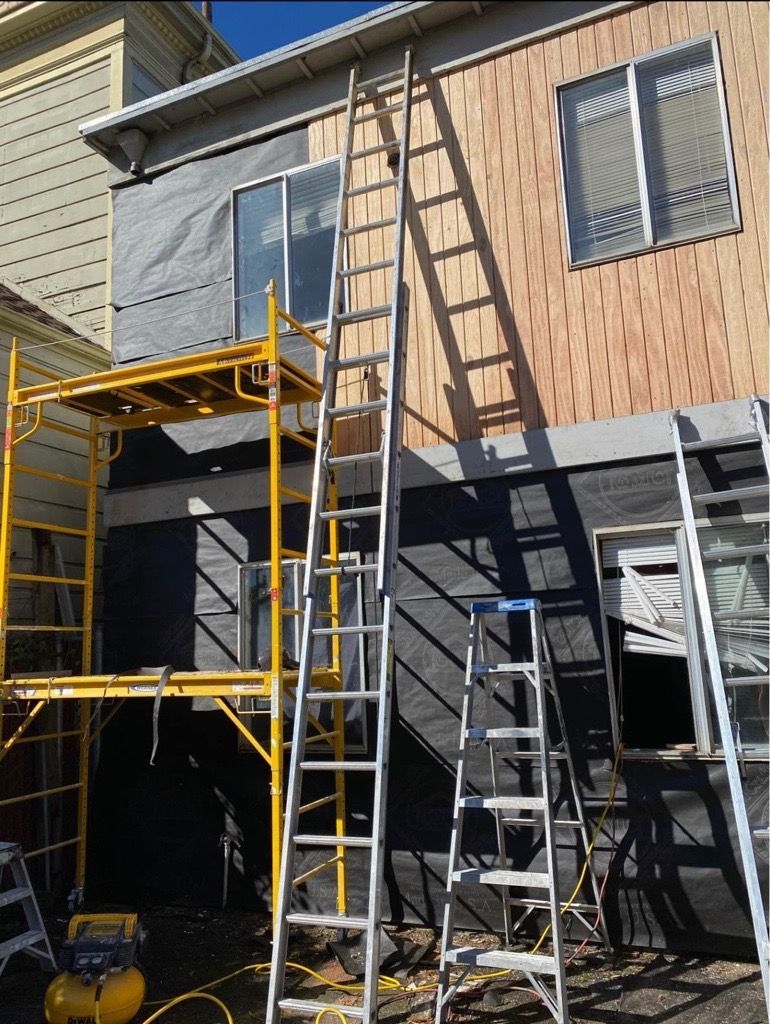 Construction site: house with scaffolding, ladders, exposed wood, and protective wrap. Yellow scaffolding, silver ladders.
