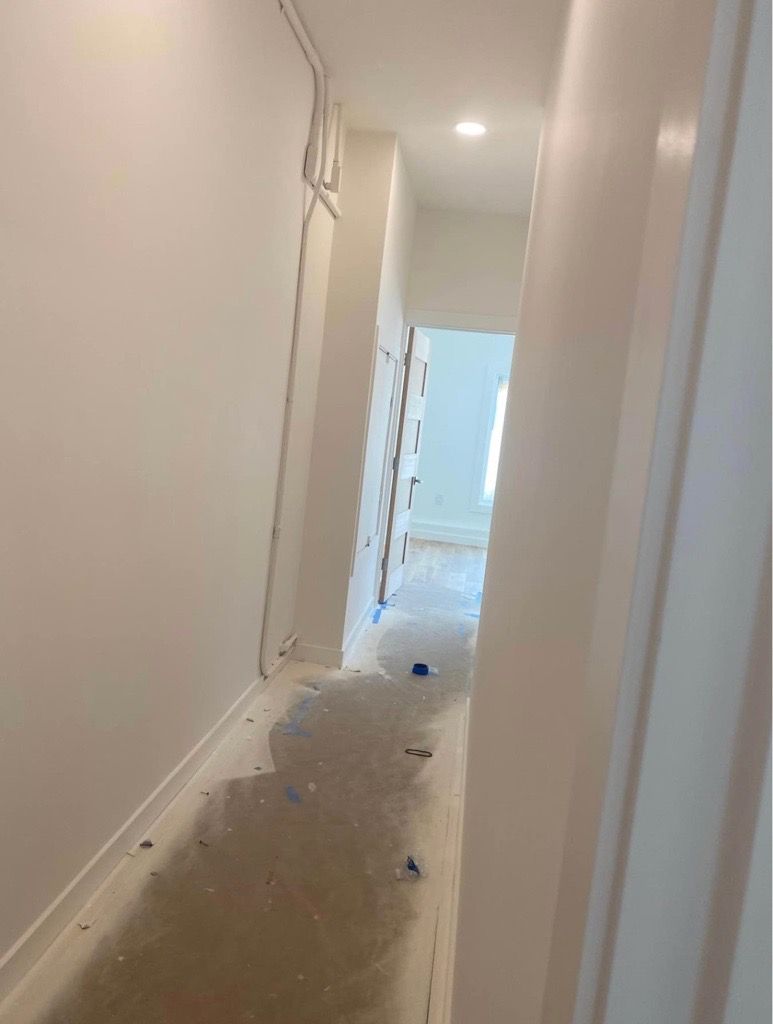 Narrow, freshly painted white hallway with construction debris on the floor, leading to a brighter room. Narrow, freshly painted white hallway with construction debris on the floor, leading to a brighter room.