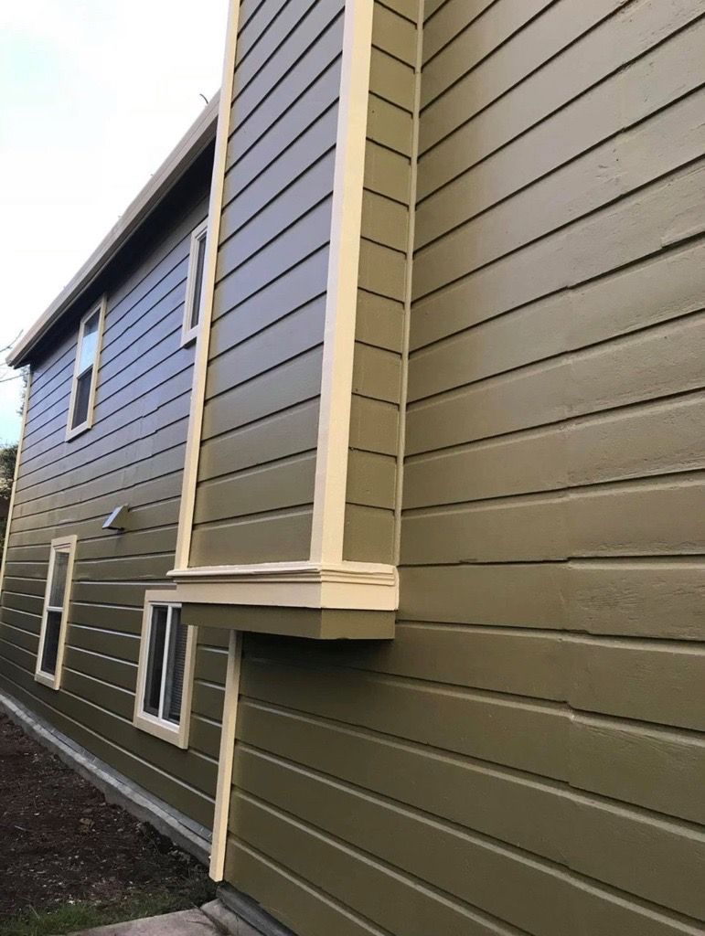 Exterior of a two-story building with green siding and cream trim. Windows and a small ledge are visible. Exterior of a two-story building with green siding and cream trim. Windows and a small ledge are visible.