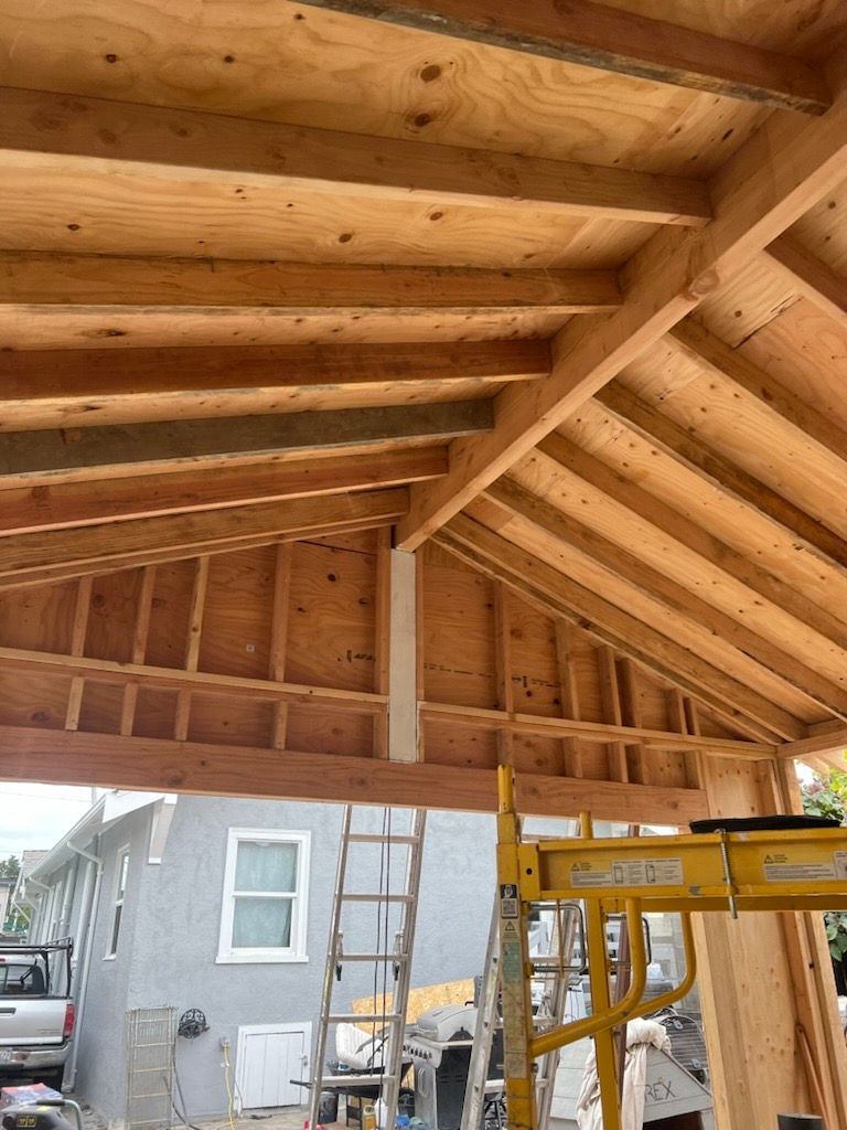 Wooden roof construction with exposed beams, house, ladder, and scaffolding in the background. Wooden roof construction with exposed beams, house, ladder, and scaffolding in the background.