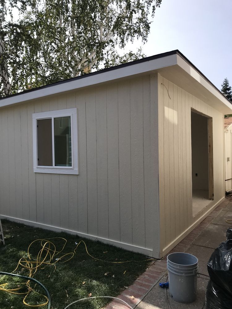 Beige-sided building with white window and door openings. Green grass, brick pathway, and bucket in yard. Beige-sided building with white window and door openings. Green grass, brick pathway, and bucket in yard.