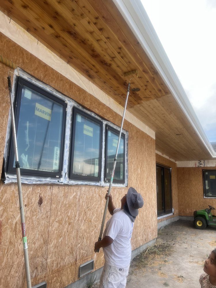 Person staining a wood ceiling from the ground using a long-handled applicator on a building exterior. Person staining a wood ceiling from the ground using a long-handled applicator on a building exterior.