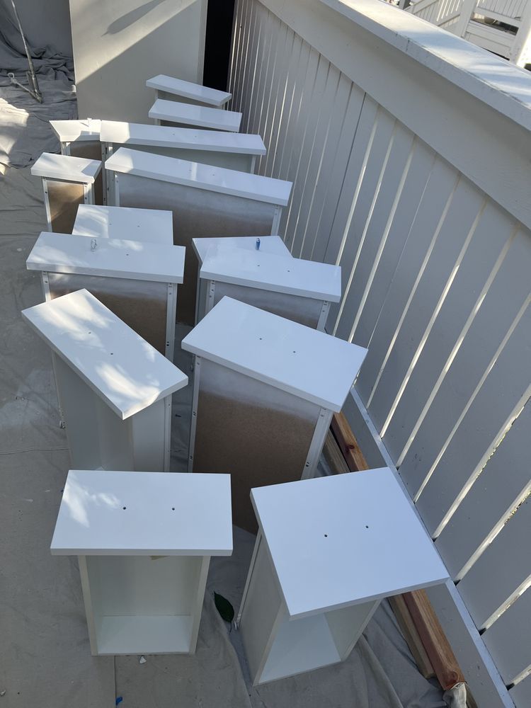White painted dresser drawers drying on a porch railing. White painted dresser drawers drying on a porch railing.