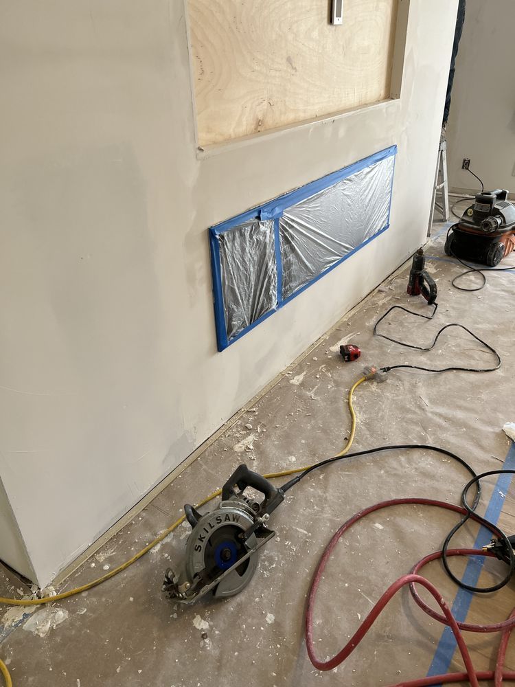 A circular saw sits on the floor near a wall with a taped-off rectangular opening under construction. A circular saw sits on the floor near a wall with a taped-off rectangular opening under construction.