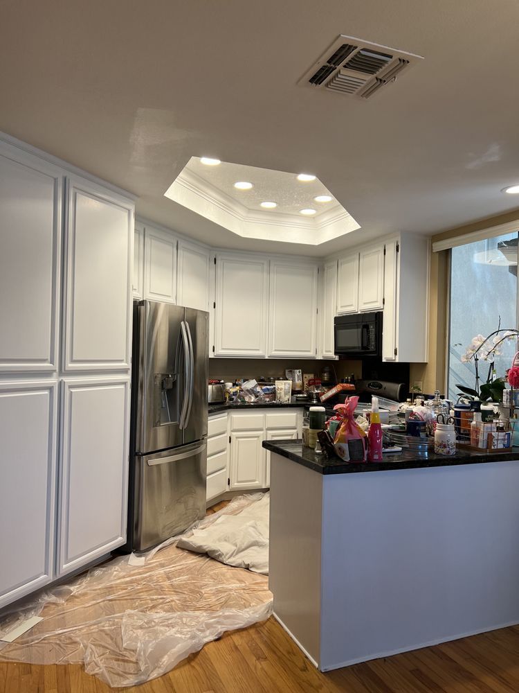 White kitchen cabinets and appliances in a room with a skylight. Painting in progress, debris on the floor. White kitchen cabinets and appliances in a room with a skylight. Painting in progress, debris on the floor.