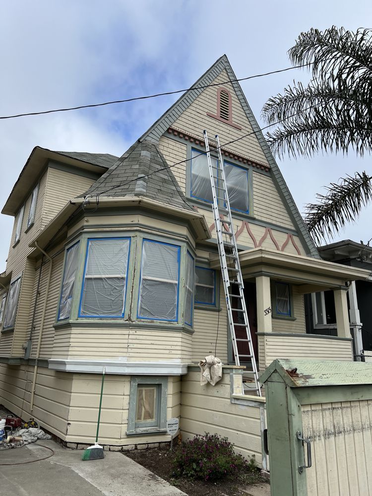 Victorian house being painted; ladder against the roof. Blue tape protects windows, cream and green trim. Victorian house being painted; ladder against the roof. Blue tape protects windows, cream and green trim.