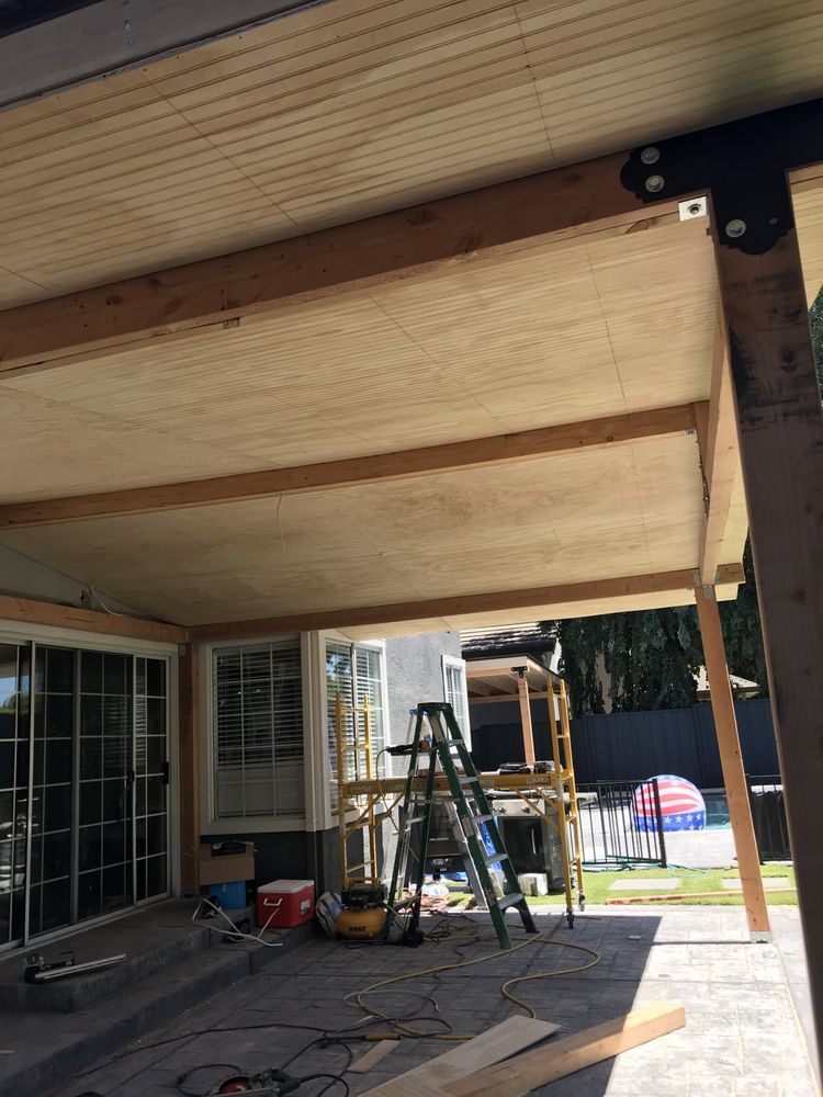 Person staining a wood ceiling from the ground using a long-handled applicator on a building exterior. Person staining a wood ceiling from the ground using a long-handled applicator on a building exterior.