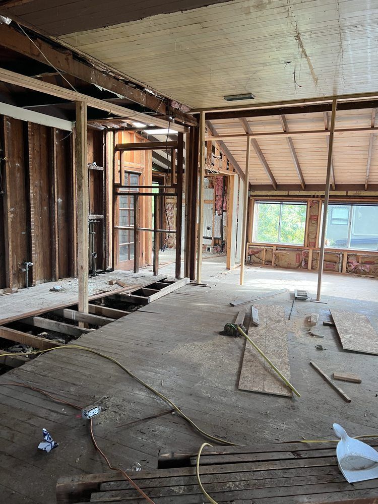 Interior of a house under construction; exposed wooden framing, bare concrete floor, and natural light from windows. Interior of a house under construction; exposed wooden framing, bare concrete floor, and natural light from windows.
