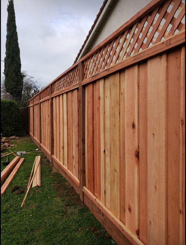 Wooden fence with lattice top running along a green lawn; cloudy sky in the background.