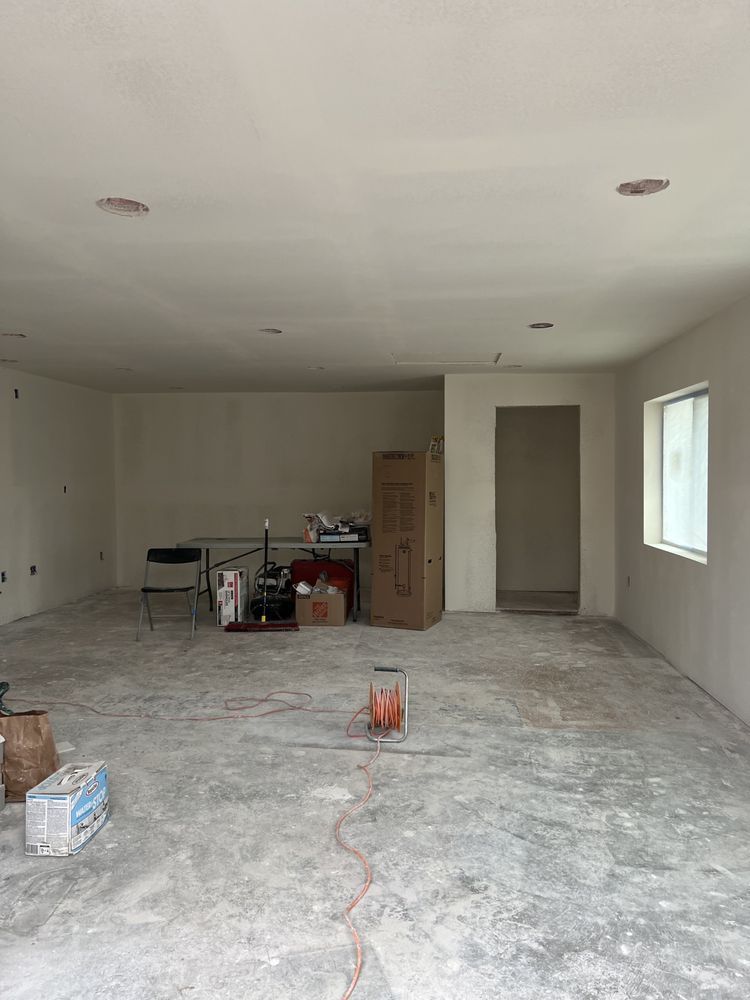 Empty, unfinished room with concrete floor, white walls, and recessed lighting. A door and a window are visible. Empty, unfinished room with concrete floor, white walls, and recessed lighting. A door and a window are visible.