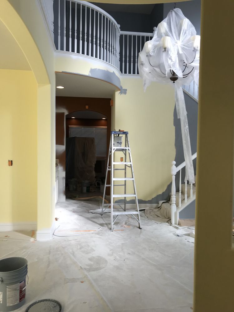Interior with yellow and gray walls, a staircase, ladder, and covered chandelier, possibly under renovation.