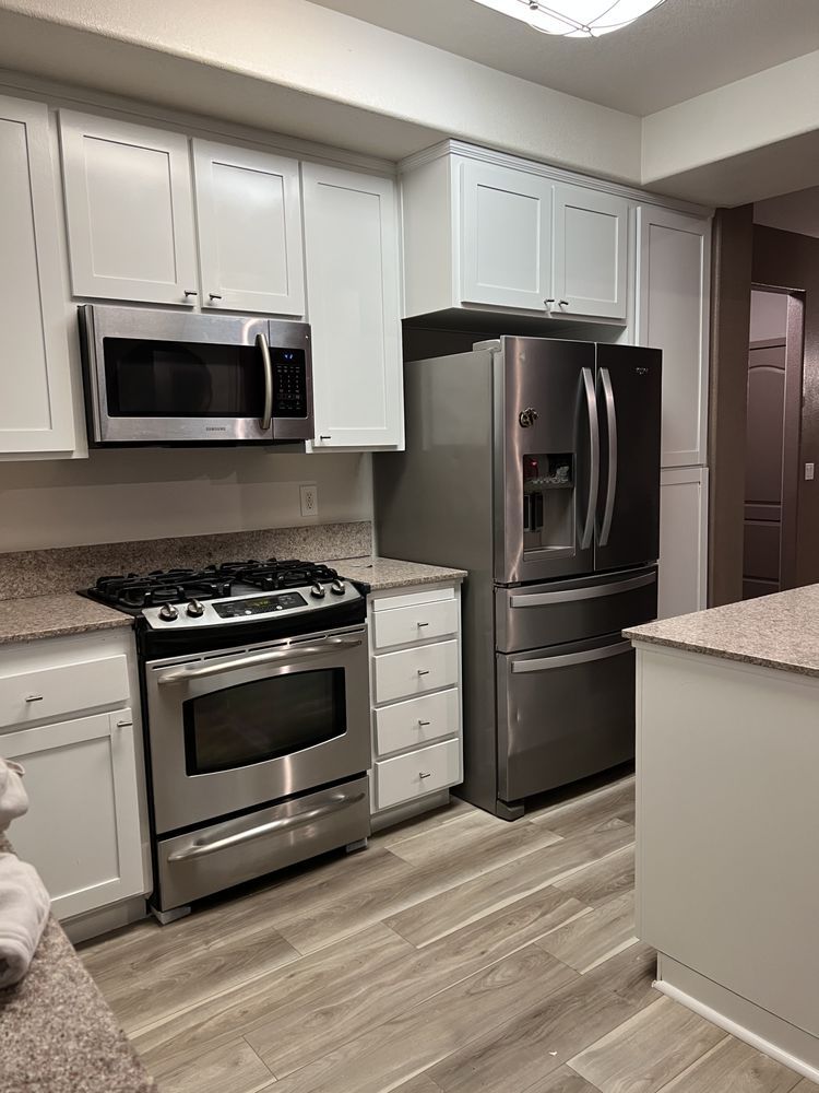 A modern kitchen with stainless steel appliances, white cabinets, and light wood flooring.