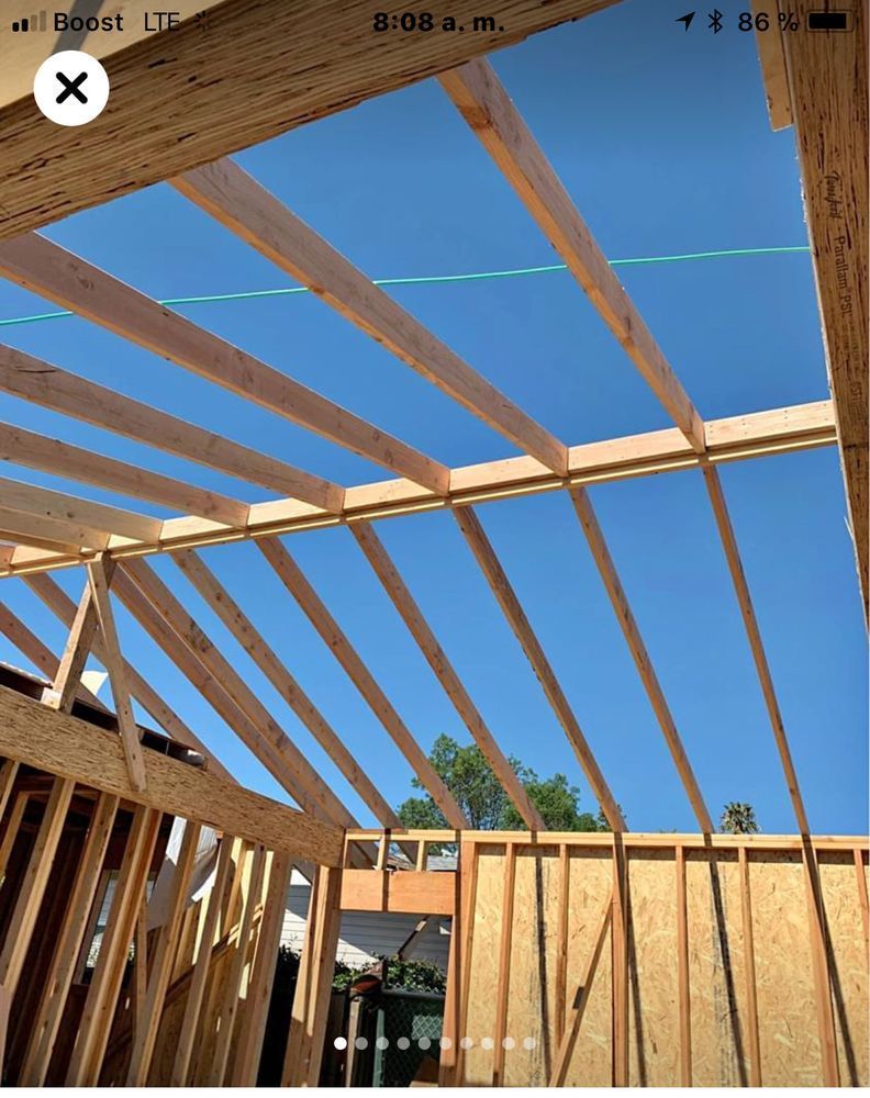 Wooden roof framing against a clear blue sky during construction.