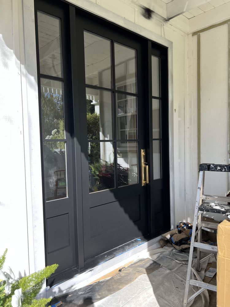 Black French doors with gold handle, white trim, on a white house exterior.