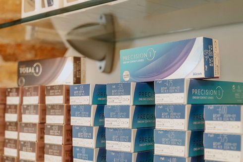 Scatole di lenti a contatto impilate sugli scaffali di un negozio. La maggior parte delle scatole sono blu e marroni.