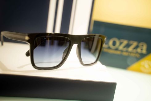 Occhiali da sole con montatura quadrata nera e lenti blu sfumate, su una superficie bianca, con una scatola con il marchio