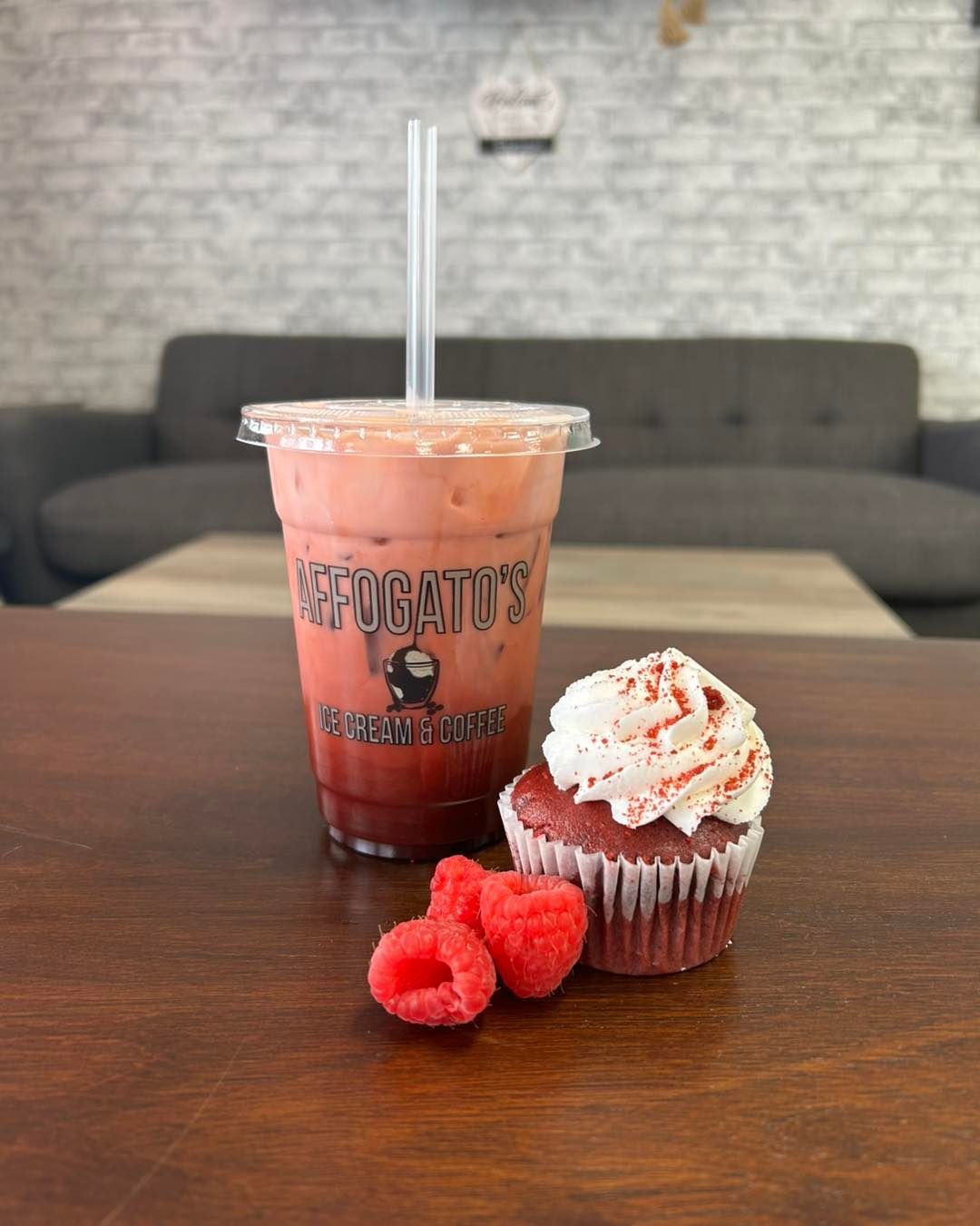 A smoothie and a cupcake with raspberries on a table.