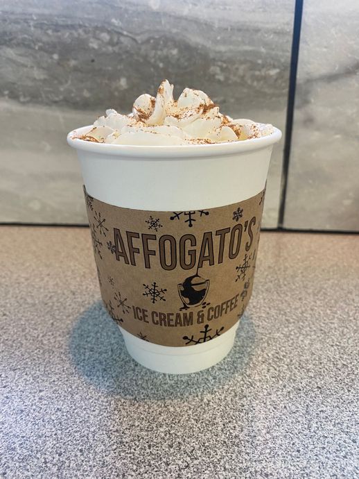 A cup of hot chocolate with whipped cream on top is on a table.
