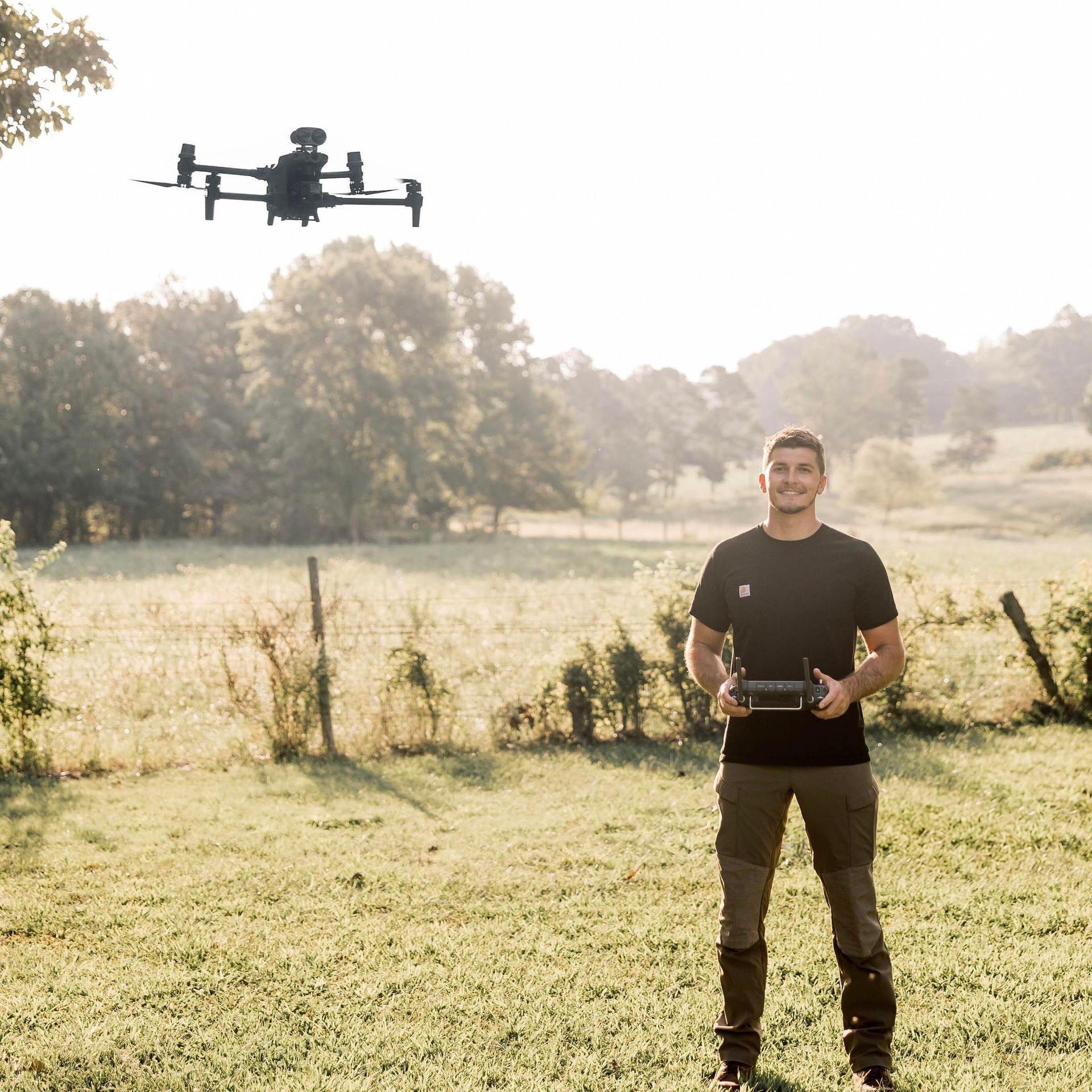 Two men pose with a harvested deer. They're sitting in tall grass, one with a rifle, both smiling, under a dark sky.