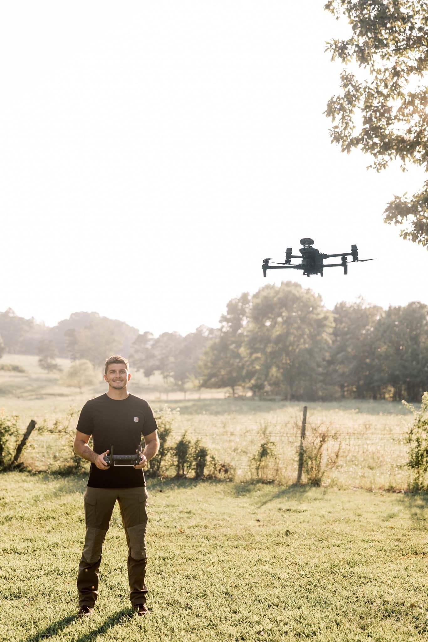 Two men pose with a harvested deer. They're sitting in tall grass, one with a rifle, both smiling, under a dark sky.