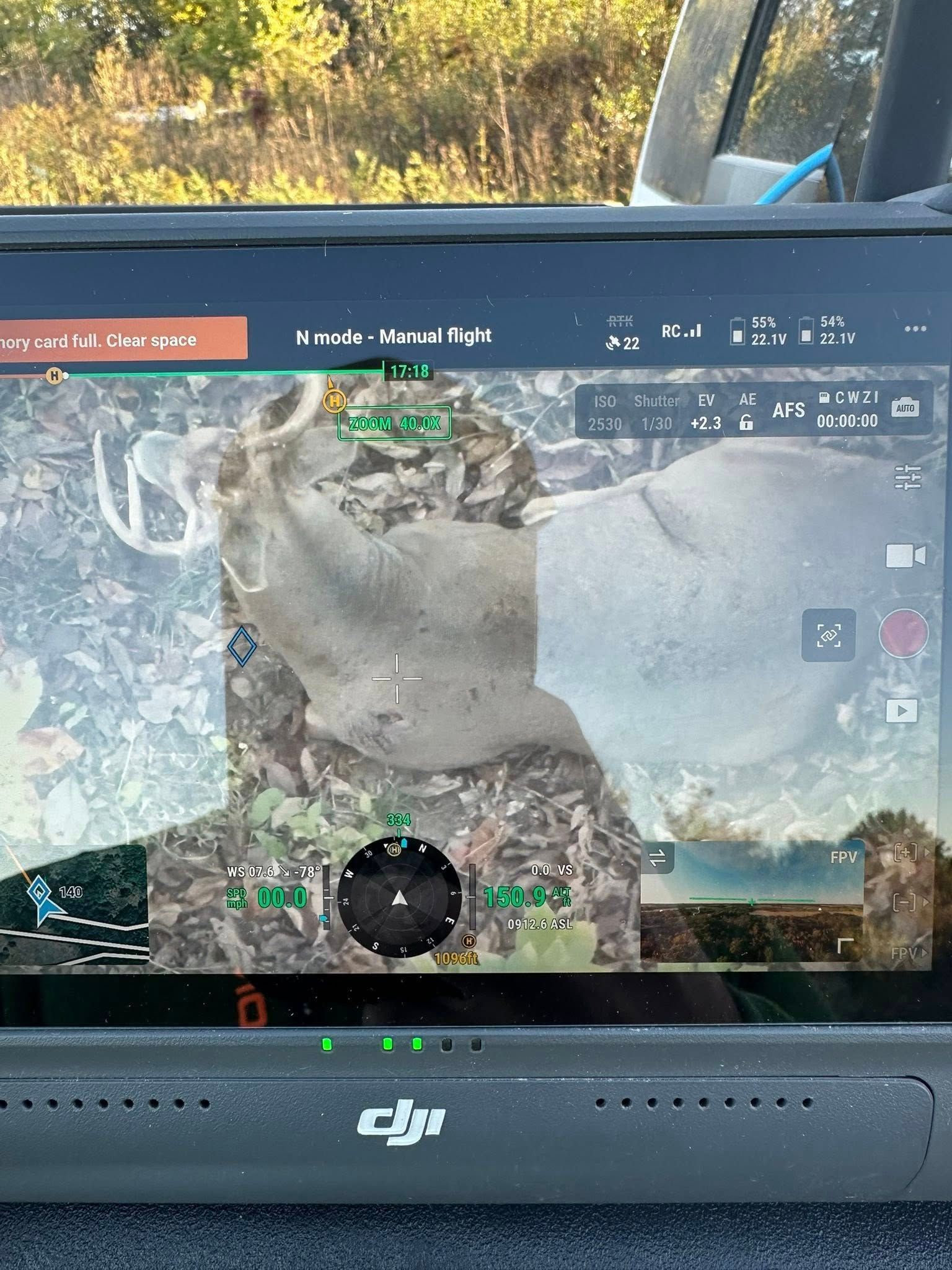 A drone controller screen displaying an overhead view of a camouflaged object in a wooded area.