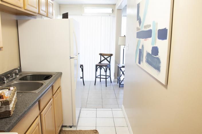 Narrow kitchen hallway leading to a bright dining area with chairs and abstract wall art