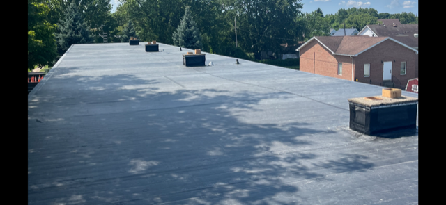 The roof of a building with a black roof and a brick building in the background.