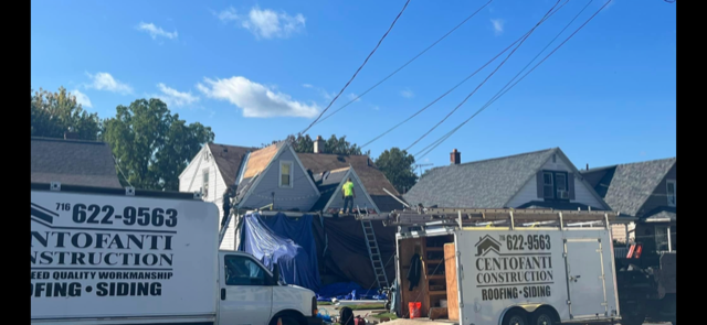 Two construction trucks are parked in front of a row of houses.