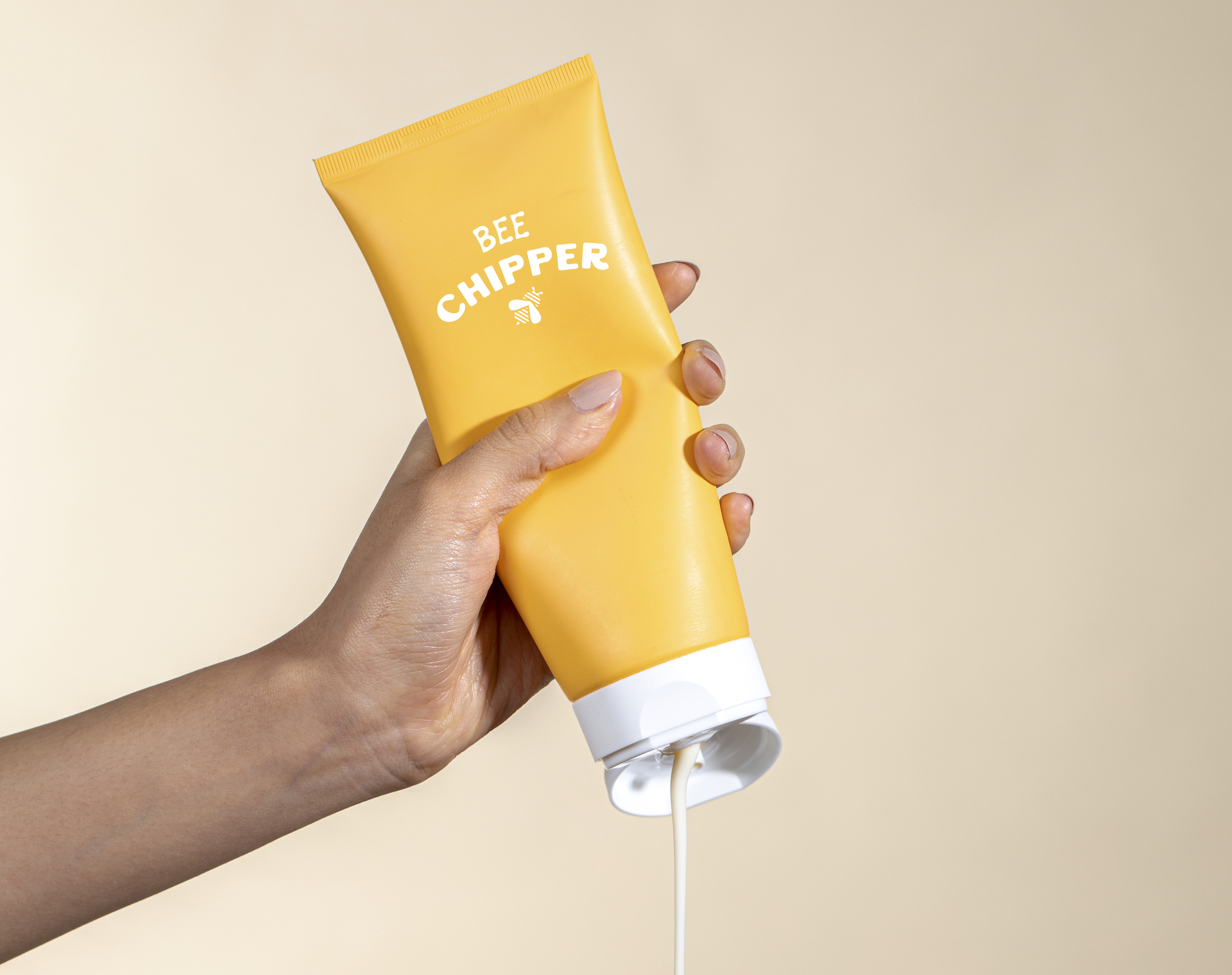 A hand squeezing a yellow tube labeled 