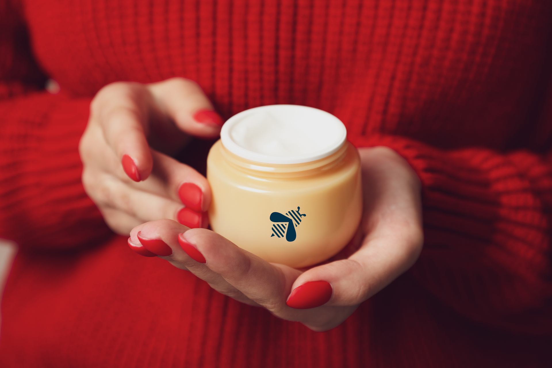 Hands holding a jar of cream; red nails, red sweater.