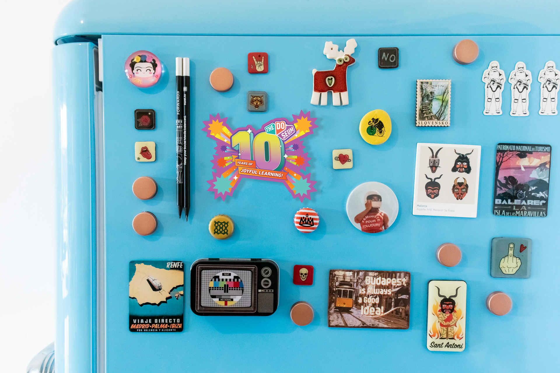 Blue refrigerator door covered in colorful magnets and a pen.