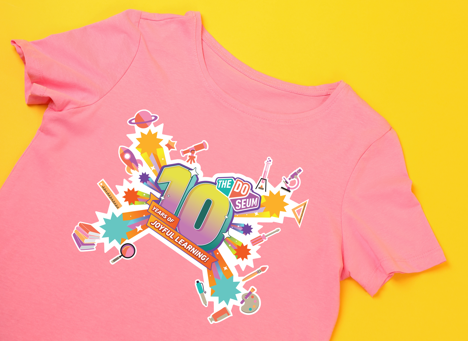 Pink t-shirt with a colorful design featuring the number 10 surrounded by science-themed illustrations.