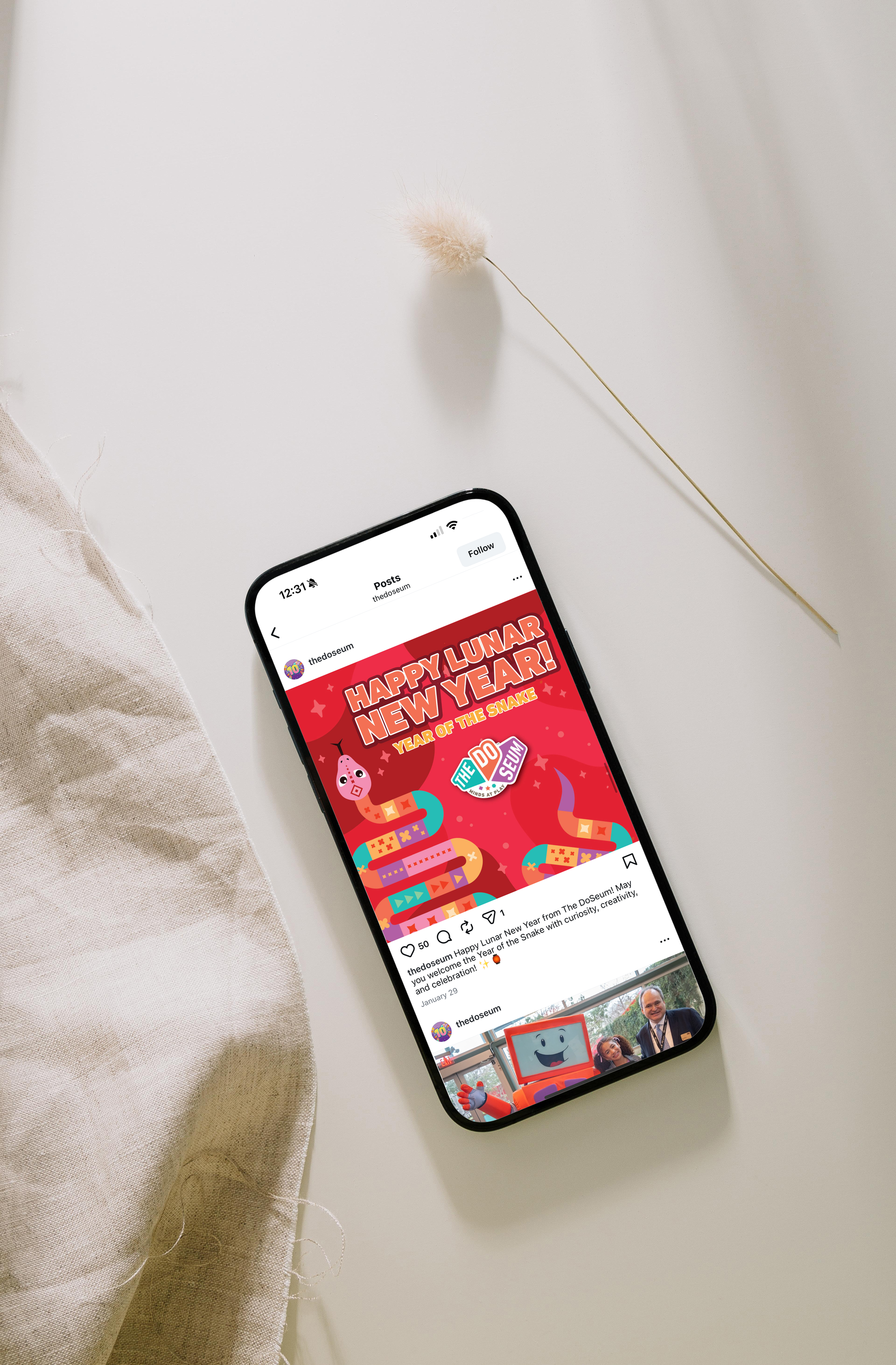 Smartphone displaying a red and pink advertisement with a white background, near a beige cloth and a dried flower.