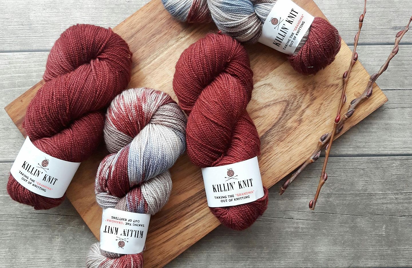 Killin' Knit skeins of red and gray speckled yarn with labels on a wooden board.