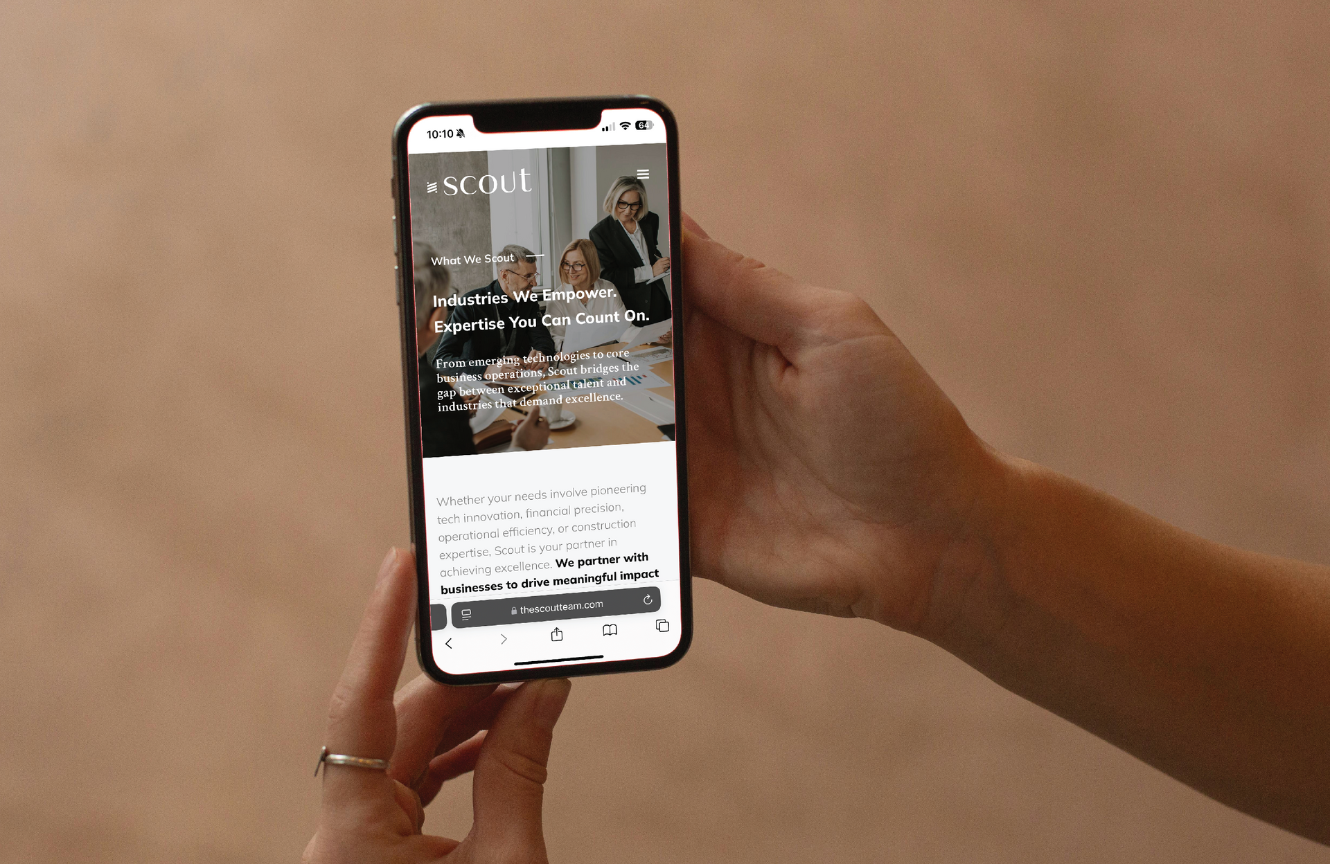 Hand holding a smartphone displaying the Scout website with business people; pink backdrop.