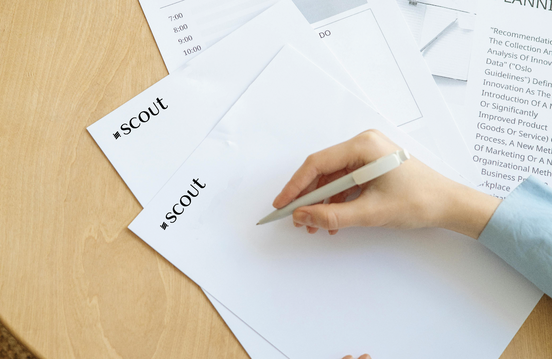 A hand holding a pen over blank paper with the word
