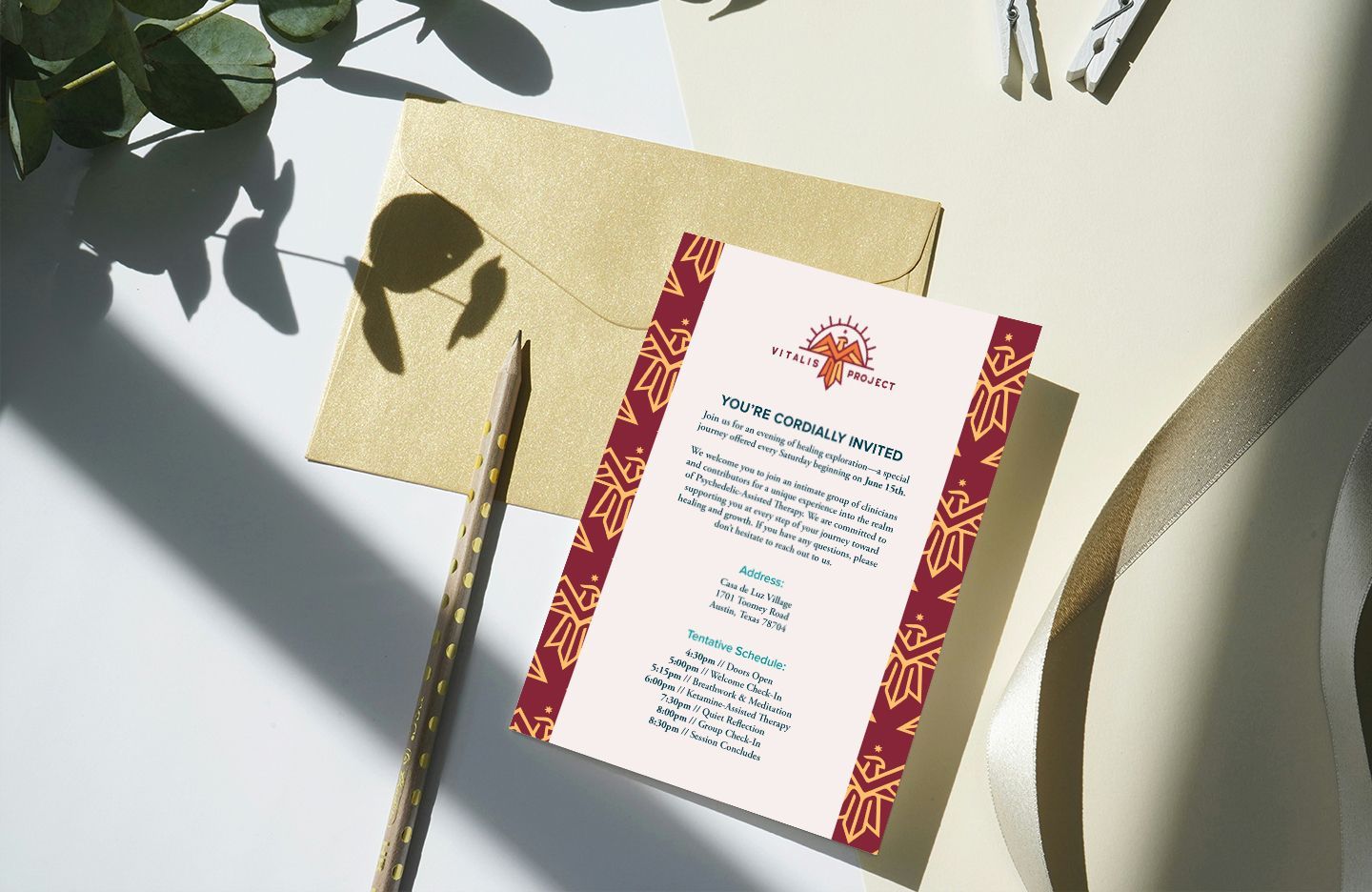 Invitation design for Vitalis Project with gold envelope, pencil, ribbon, and greenery on white surface.