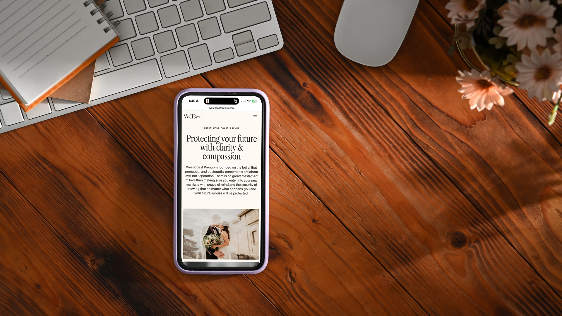 Smartphone displaying text on a wooden desk with a keyboard, mouse, notepad, and flowers.