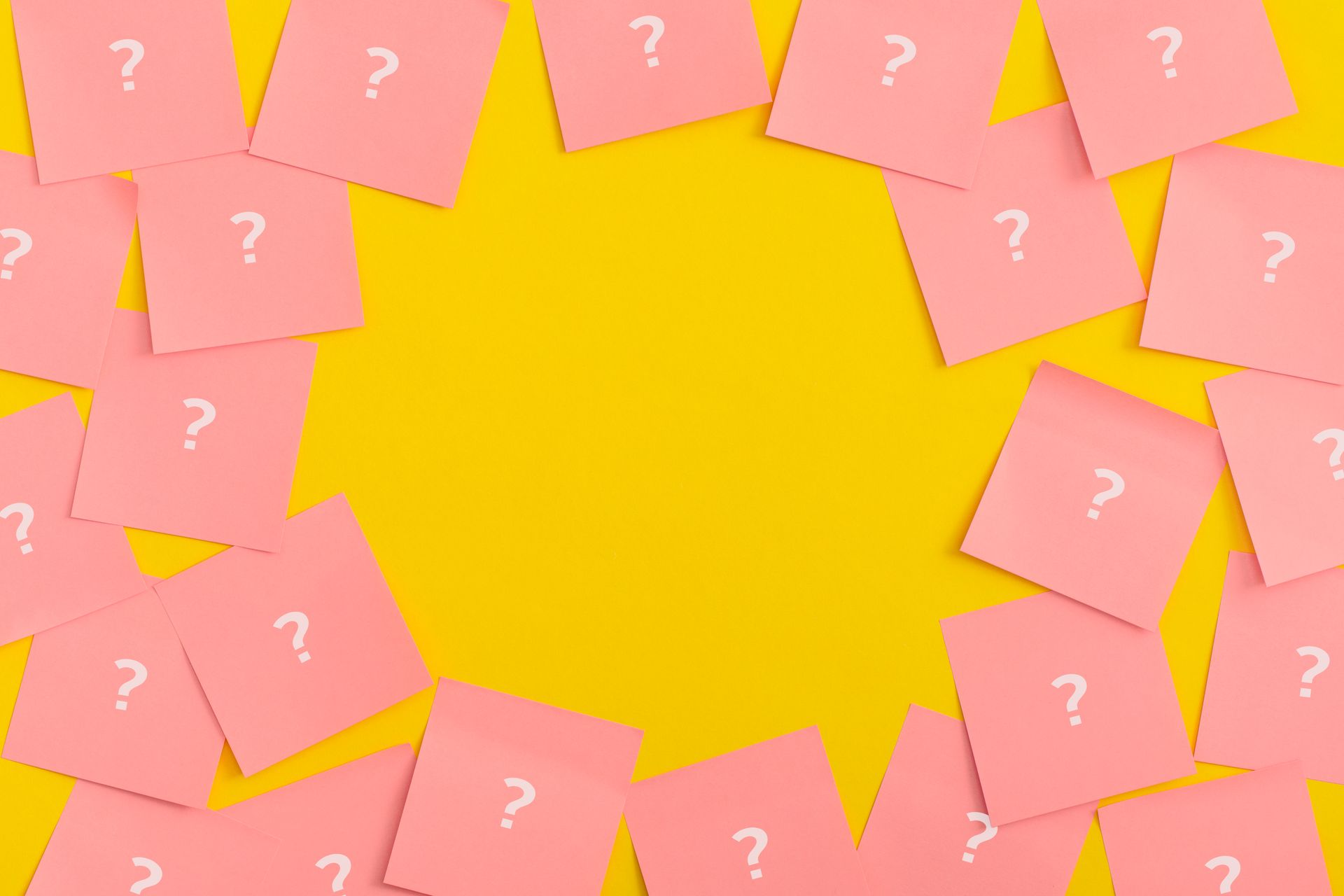Pink sticky notes with white question marks scattered on a yellow background, framing an empty space.