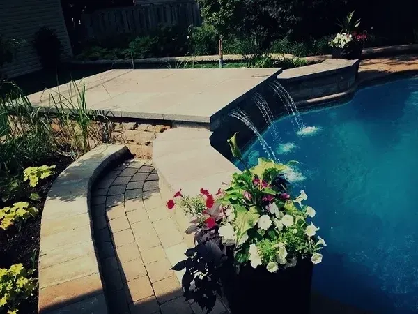 Une piscine avec une cascade et des fleurs devant