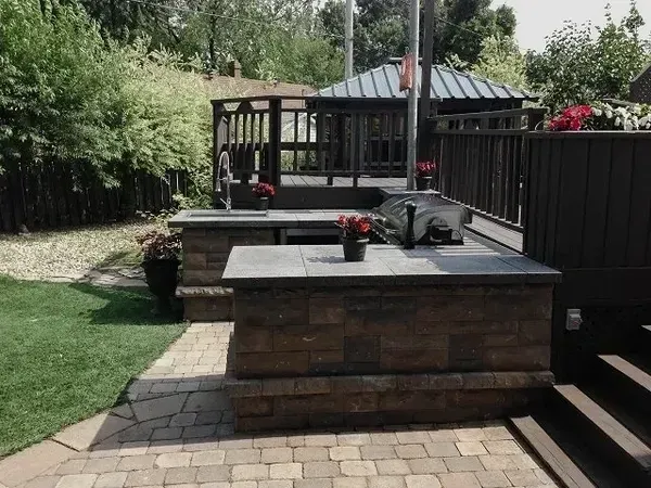 Un patio en brique avec un grill et un belvédère en arrière-plan