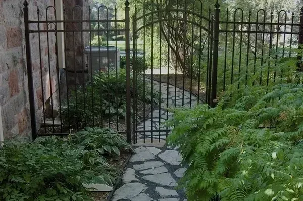 Une passerelle en pierre menant à un portail en fer forgé dans un jardin.