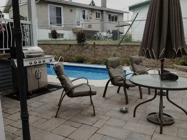 Un patio avec chaises, table et parasol devant une piscine